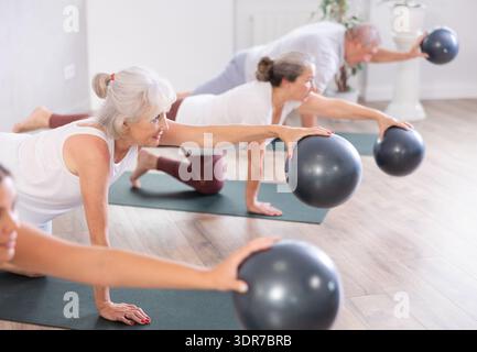 Gruppe reifer aktiver Menschen, die während des Pilatesurses in der Gruppe im Fitnesscenter Softballübungen machen Stockfoto