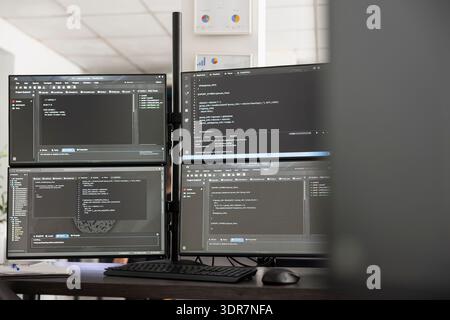 Ein leeres Startup Office zeigt mehrere Computerbildschirme mit Softwarecode und digitalen Informationen an. Clean Workspace steht für Backend-, Frontend- und Cloud-Entwicklung in modernen Workspaces. Stockfoto