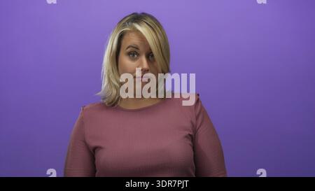 Die junge blonde Frau zeigt ihren Zeigefinger in einem violetten Studio-Setting nach oben, was keine Geste anzeigt; Ablehnung. Stockfoto