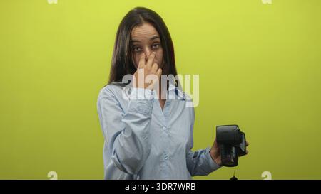 Frau in hellblauem Hemd, die Kamera mit dem Finger in der rechten Hand in einem hellgrünen Studio hält; ernste Warnung. Stockfoto