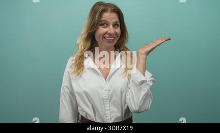 Die Frau zeigt mit dem Finger auf die Handfläche in blaublauem Hintergrund des Studios und trägt weißes Hemd und Gürtel; fröhliches Selbstvertrauen. Stockfoto