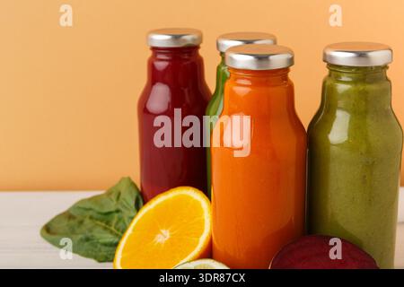 Frische Obst- und Gemüsesäfte in Glasflaschen mit orangefarbenem Hintergrund und geschnittenen Früchten Stockfoto