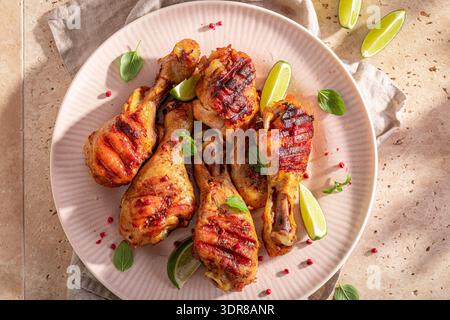 Scharfe gebratene Hähnchenkeule, serviert mit Limette und Kräutern. Gegrillte Hähnchenschenkel mit Kräutern und Gewürzen. Stockfoto