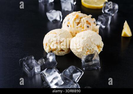 Drei Kugeln Eis mit Zitronenscheiben und Eiswürfeln auf dunkler Oberfläche Stockfoto