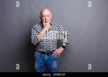 Ein älterer Mann in kariertem Shirt posiert nachdenklich vor grauem Hintergrund Stockfoto