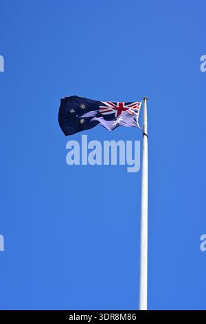 Australische Nationalflagge, die am Fahnenmast fliegt und im Wind gegen klaren blauen Himmel flattert Stockfoto