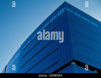 Zeitgenössischer Glashochhaus mit schlanker geschwungener Fassade vor blauem Himmel. Moderner Firmenturm mit elegantem architektonischem Design und reflektierender Oberfläche Stockfoto