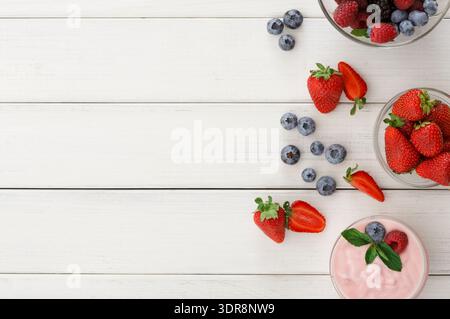 Frischer Obstsalat und Joghurt auf einem Holztisch mit bunten Beeren und Erdbeeren Stockfoto