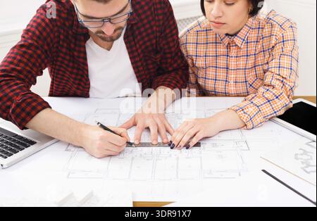 Zwei Personen arbeiten zusammen an einem Architekturplan in einem hellen Innenraum Stockfoto