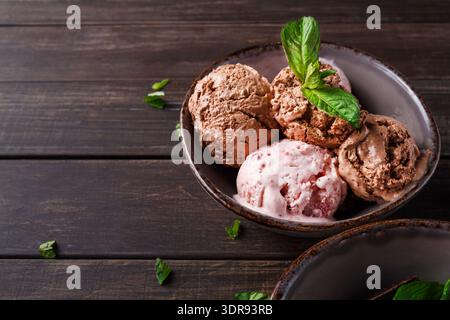 Verschiedene Eissorten stehen in einer Schüssel auf einem Holztisch mit Minzblättern daneben Stockfoto