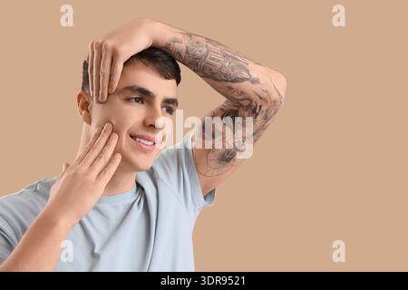 Junger Mann, der Gesichtsaufbauübung auf beigefarbenem Hintergrund macht Stockfoto