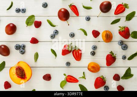Sammlung von Früchten und Beeren auf einer Holzfläche in einem farbenfrohen Layout mit Grün angeordnet Stockfoto