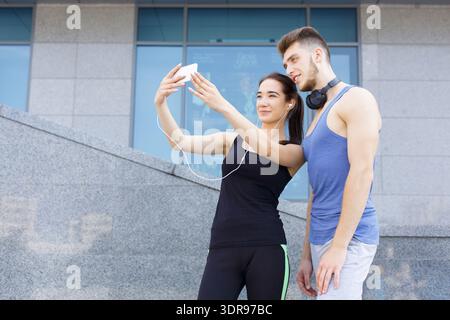 Ein Paar nimmt Selfie zusammen auf Treppen in Urban Area während des Sonnentages, während es Musik hört Stockfoto