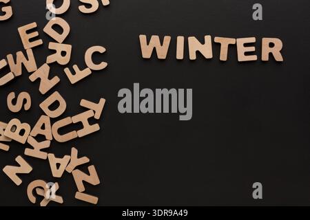 Holzbuchstaben, die auf einer schwarzen Oberfläche verstreut sind, beschreiben Winter und andere Buchstaben Stockfoto