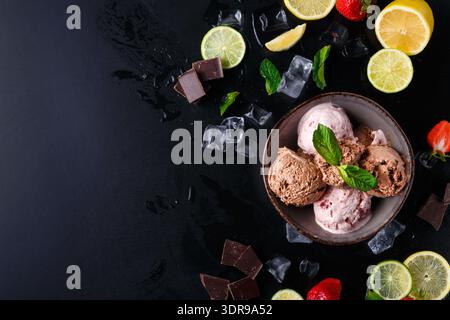 Verschiedene Geschmacksrichtungen von Eis in einer Schüssel mit Obst und Schokolade auf dunklem Hintergrund Stockfoto