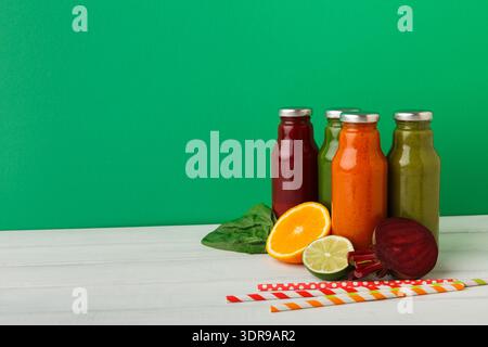 Bunte Saftkollektion auf einem Tisch mit grünem Hintergrund und frischen Zutaten in der Nähe Stockfoto