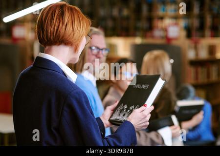 Kaukasische Frau mittleren Alters, die Buch hält, während sie in der Reihe steht Stockfoto