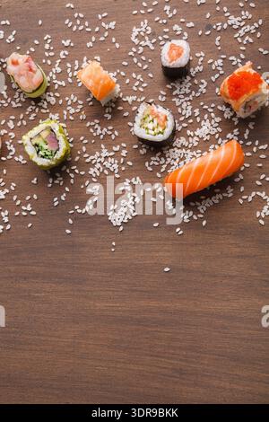 Sammlung von Sushi-Stücken auf Holzoberfläche mit verstreuten Reiskörnern Stockfoto
