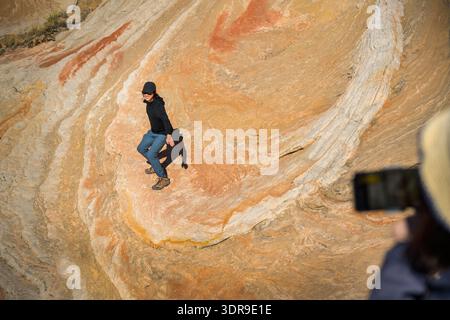 Junger Mann, der Surfposien auf den wirbelnden Felsen bei White Pocket macht. Unscharfe Frau, die Fotos macht. Vermilion Cliffs National Monument. Arizona. USA Stockfoto