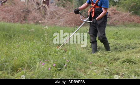 Ein Mann mäht das Gras an einem Sommertag mit einem Trimmer. Stockfoto