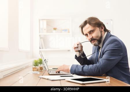 Professioneller Mann, der am Schreibtisch arbeitet, während er die Kamera in einem modernen Büro betrachtet Stockfoto