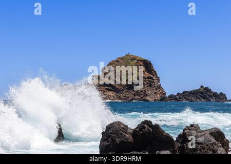 Die felsige Atlantikküste in der Nähe von Porto Moniz Madeira Portugal explodieren mächtige Wellen gegen dunkle vulkanische Felsen und ein zerklüfteter Meeresstapel erhebt sich vor der Küste b Stockfoto
