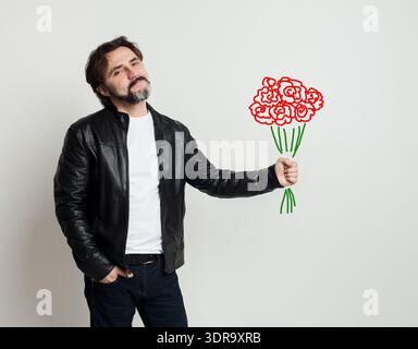 Der Mann hält eine Zeichnung von Blumen in der Hand, während er vor einem Ebenen Hintergrund steht Stockfoto