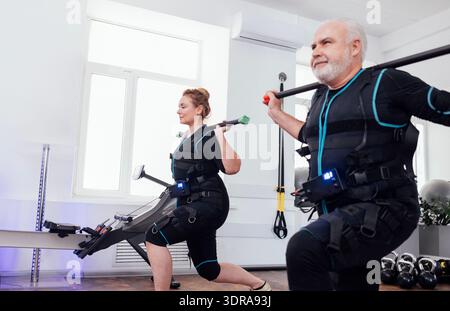 Älteres Sportpaar in ems-Anzügen, das elektrische Muskelstimulationstraining mit Gymnastikstöcken macht Stockfoto