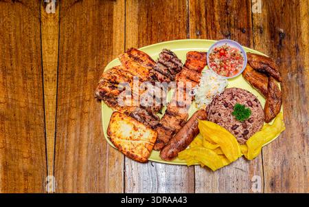 Gegrillte Fleischsorten mit Reis, gebratenem Käse und Tomatensalat, Teller mit verschiedenen Grillsorten auf Holztisch, Stockfoto