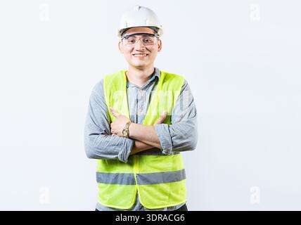 Porträt eines gutaussehenden und lächelnden Ingenieurs mit gekreuzten Armen isoliert. Porträt eines jungen, fröhlichen Ingenieurs in Helm und Weste i Stockfoto