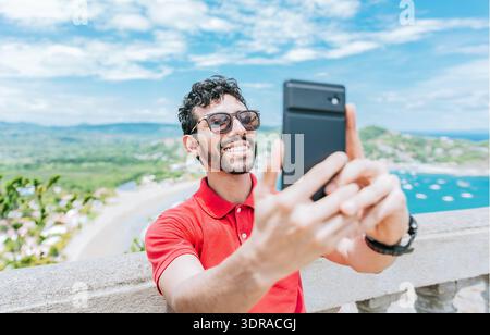 Glücklicher Tourist, der ein Selfie an einem Aussichtspunkt am Strand macht. Gutaussehender Mann, der ein Selfie am Aussichtspunkt von San Juan del Sur macht Stockfoto