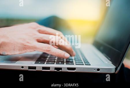 Nahaufnahme der Hände einer Person auf der Laptop-Tastatur im Freien, Nahaufnahme der Hände eines Mannes, der an seinem Laptop arbeitet. Seitenansicht der Hand Stockfoto