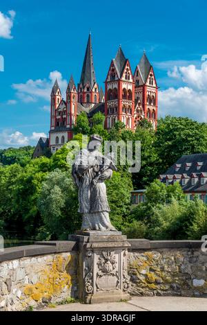 Eine verwitterte Statue von Johannes Nepomuk mit der Kathedrale von Limburg im Hintergrund bei schönem Sommerwetter Stockfoto