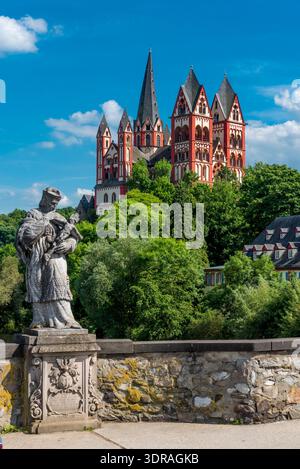 Eine verwitterte Statue von Johannes Nepomuk mit der Kathedrale von Limburg im Hintergrund bei schönem Sommerwetter Stockfoto