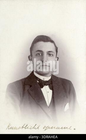 Dieses Studio-Foto von Adriaan Boer, aufgenommen zwischen 1897 und 1912 in Baarn, Niederlande, zeigt ein Nahporträt eines Mannes mit dunklem, geschliffenem Haar, der Jacke, Weste, Fliege und Taschentuch trägt. Das Foto ist eine „Carte de Visite“ und enthält eine handschriftliche Notiz, die auf die künstliche Lichtbelichtung hinweist. Das Bild dokumentiert niederländische Studiofotografie, Herrenmode, Porträttechniken und fotografische Methoden des frühen 20. Jahrhunderts. Stockfoto