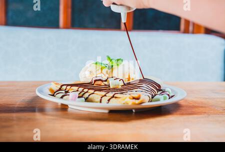 Schokoladen-Krepp mit Eis auf hölzernem Hintergrund. Nahaufnahme von süßem Crepe mit Eis Stockfoto
