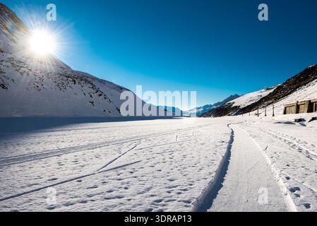 Die Sonne blickt hinter einer Bergwand in einem schneebedeckten Hochtal in den Schweizer Bergen hervor Stockfoto