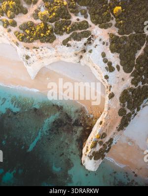 Aus der Vogelperspektive treffen Sie auf das türkisfarbene Meer und schaffen einen atemberaubenden Kontrast von Texturen und Tönen im berühmten Praia da Marinha, Praia da Marin Stockfoto