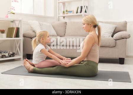 Yoga-Session zu Hause mit Mutter und Tochter, die gemeinsam auf einer Matte im Wohnzimmer üben Stockfoto