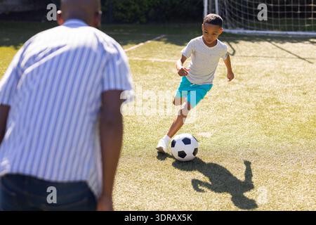 Fußball spielen, Enkel dribbelt auf dem Feld, Großvater beobachtet aufmerksam Stockfoto