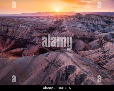 Atemberaubender Blick aus der Luft auf lebendige geologisch geschichtete Sedimentgesteinsformationen während des goldenen Sonnenuntergangs im Altyn Emel Nationalpark, Kasachstan Stockfoto