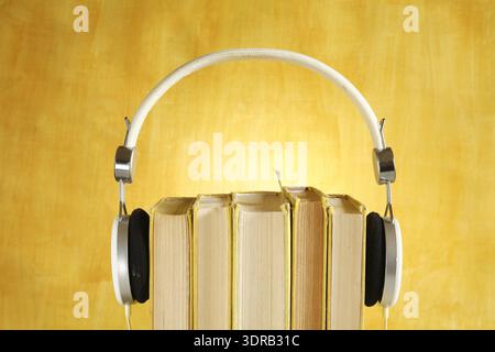 Hörbuch-Konzept mit Büchern und Kopfhörern auf verschwommenem, glattem gelbem Hintergrund Stockfoto