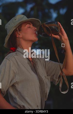 Malediven. Eine junge Frau im Safarianzug trinkt aus einer Wasserflasche. Stockfoto