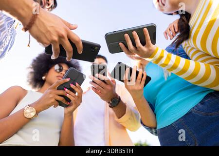 Gruppe verschiedener Freunde, die Smartphones halten, Inhalte im Freien teilen und diskutieren. Soziale Netzwerke, Technologie, Mobilgeräte, Kommunikation, Enterta Stockfoto