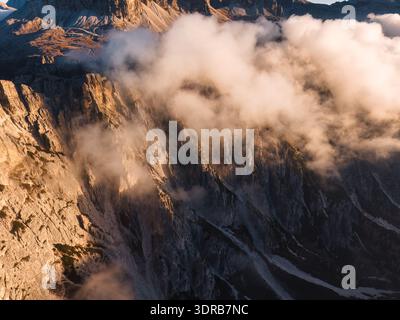 Atemberaubender, rauer Kalksteinberg und tiefes Tal, bedeckt mit goldenem Nebel während des Sonnenaufgangs in den Dolomiten, Italien Stockfoto