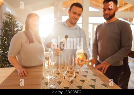 Ein lächelnder junger Mann gießt Champagner in Gläser im Speisesaal des Hauses. Stockfoto