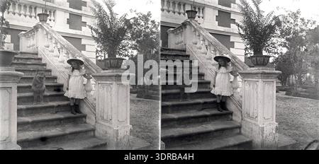 Ein Stereophotogramm von 1904–1907 zeigt ein Mädchen mit Hund auf den Stufen des großen Kolonialhauses von J. G. Mulder an der Ecke Boulevard Bonnal und Rue de Cherbourg in Haiphong, Indochina (heute Vietnam). Der Hund gehört Mulder. Das Bild dokumentiert koloniale Architektur, häusliches Leben, Haustiere, Kinder, europäische Einwohner, Kolonialgesellschaft des frühen 20. Jahrhunderts, Personal im Haushalt und visuelle Dokumentation der häuslichen Umgebung. Stockfoto
