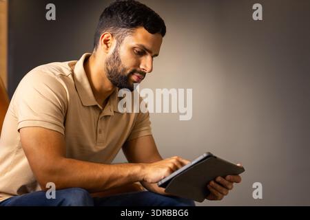 Mit Tablet, Mann sitzt drinnen und fokussiert auf den Bildschirm, Kopierraum Stockfoto
