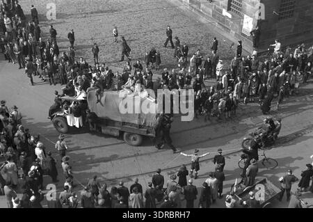 Am 8. Mai 1945 jubelte eine Menge alliierte Militärfahrzeuge der Seaforth Highlanders of Canada in der Nähe des kaum sichtbaren Königspalastes am Damm in Amsterdam. Krankenschwestern sind auf die Fahrzeuge geklettert und Rote Kreuze sind im Vordergrund sichtbar. Fotografiert vom Pfarrhaus Nieuwe Kerk, dokumentiert das Bild die städtische Feier, die zivile Interaktion mit Militärkräften und die Befreiung der Stadt. Stockfoto