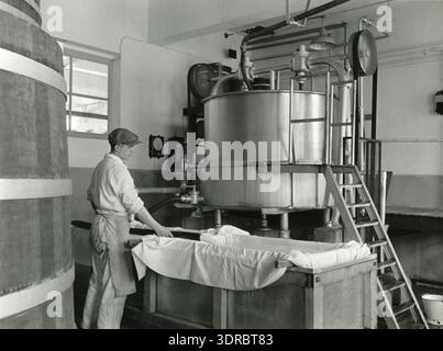 Dieses Foto zeigt die Textilindustrie in den Niederlanden am 7. April 1938 und zeigt die Produktion von Wolle aus Milch (Kasein) in Betrieben wie Casenka oder AKU. Das Bild zeigt die frühen industriellen Prozesse zur Umwandlung von Kasein in Textilfasern, Maschinen, Lagerung, Rohstoffe und die Rolle chemischer Textilien in der niederländischen Industrie in den 1930er Jahren Arbeiter und Produktionslinien demonstrieren historische Textilverarbeitungstechniken. Stockfoto